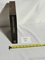 Book spine with title 'ARISTOTLE ETHICS' and Folio Society emblem, alongside measuring tape showing about 10 inches in height