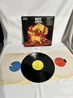 Photo of the album cover and three vinyl records laid out, showing colored center labels and the album artwork with an explosion.