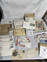 Wide view of the collection showing stacks of first day cover envelopes, vintage stamped envelopes, and various postal items arranged on white background