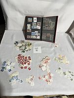 Overview photo showing piles of mostly loose used stamps organized by color, and a black stamp stockbook open with some stamps mounted inside sleeves