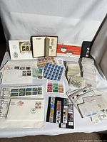 Overview of large collection of stamps, first day covers, loose stamps in envelopes, and collectors sheets spread out on white surface under neutral lighting.
