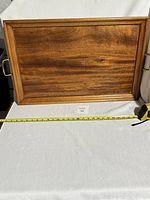 Rectangular wooden serving tray with brass handles on sides set against white cloth background and tape measure showing width dimension of about 21.5 inches.