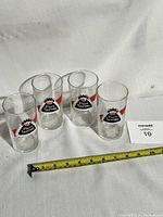Four vintage Pure Spring Ginger Ale soda pop glasses arranged in a row on a white surface with a measuring tape showing approximate height.