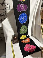 Buddha statue seated with black batik 7 chakra cloth hanging behind on white fabric background with measuring tape.