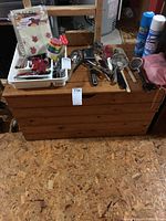 Wooden chest with various kitchen utensils and items on top, on a textured brown floor, against a basement wall including shelves and water heater.