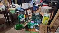 Photo showing various gardening items including a metal cart with ceramic planter, garden hoses, weed killer containers, and other garden supplies on and around a table.