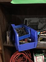Photo showing blue plastic storage bin packed with small screws, nuts, bolts, and other fasteners on wooden shelving.