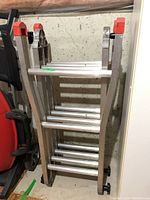 Folded multi-position aluminum ladder showing locking hinges and red plastic end caps, aluminum tubular construction.