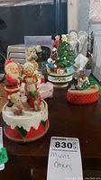 Photo showing seven assorted music boxes including three with Christmas themed figurines like Santa, child, reindeer, Christmas tree, angels, and dogs.