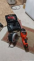 Image showing Craftsman circular saw, Black and Decker hedge trimmer, and Skil jigsaw on floor with carrying case.