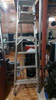 Full view of six foot aluminum step ladder standing upright in basement setting.
