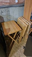 Photo of five pine TV tables in basement. Tables have a light pine finish, folding leg mechanism. Two remain unopened in packaging.