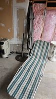 Collapsible lawn chair with green and white striped fabric, umbrella stand and closed umbrella beside it in unfinished room