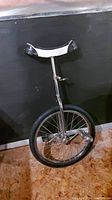 Full view of the unicycle showing the metal frame, black and white seat with tape on edges, single tire and pedals.