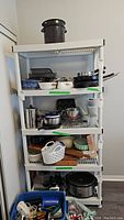 Front view of white resin utility shelf filled with kitchen cookware, utensils, and small appliances.