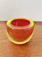 Front view of Sommerso glass ashtray showing red interior and yellow exterior on wooden surface