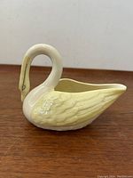 Side angle view showing smooth white swan body and detailed iridescent yellow wings.