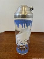 Clear glass cocktail shaker with white and blue enamel polar bear and icicle decoration, viewed from top down to show metal screw-on lid with spout.