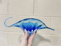 Side angle view of blue abstract glass bowl showing upward curving ends and ribbed fan pattern inside.