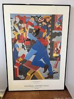 Full view of the framed colored poster titled 'The Builders' by Jacob Lawrence for National Lawyers Guild with geometric abstract figures at work.