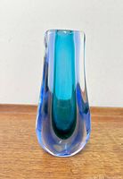 Front view of aqua blue and green Sommerso Murano glass vase on wooden surface against white wall.