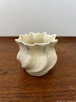 Front view of cream colored Belleek vase showing wavy rim and twist shell-like texture, 3 inches tall.