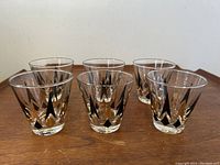 Photo showing all six glasses arranged in two rows on a wooden surface, clear glass with black and gold peak pattern.