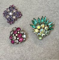 Three vibrantly colored Art Deco rhinestone brooches laid out on fabric background displaying colors and design.
