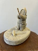 Front view showing fisherman in hooded parka standing in oval boat with fishing line and fish.