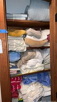 Closet shelves filled with folded towels, sheets, pillowcases, and bedspreads in assorted colors and patterns.
