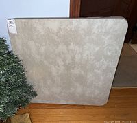 Top-down view of the folding card table showing the textured beige and gray surface with wear.