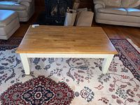 Wood coffee table with natural wood segmented top and white painted legs on a patterned rug in a living room.