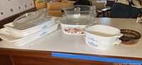 Full view of all casserole dishes and lids on countertop showing variety of Corning Ware patterns and sizes.