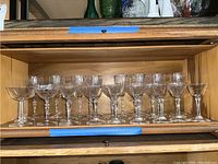 Wide view of 15 crystal glasses arranged in a wooden cabinet shelf showing the etched floral and geometric designs.