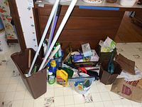 Photo showing mop buckets, brooms, mop handles, and various cleaning products in containers and bottles
