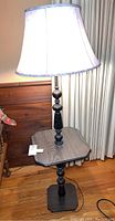 Full view of wooden floor lamp with attached side table and turned wooden pole base, showing structure and design.