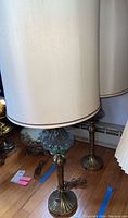 Full view of two tall brass base table lamps with cream fabric shades on hardwood floor.