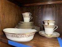 Cup, saucers, plates, and serving bowl arranged on wooden shelf showing the pattern and condition