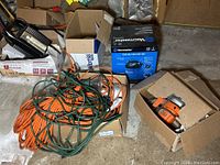 Photo showing mini wet/dry vacuum box, Black & Decker saw in a box, and tangled orange and green extension cords.