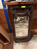 Full view of the wood-framed mirror with four iron coat hooks attached at the top and bottom, standing on a basement floor with visible scratches.