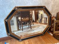 Full view of the octagonal wall mirror showing black and gold ornamental frame, mirror surface with some wear.
