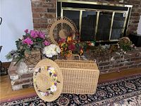 Wide shot showing picnic basket, decorated straw hat, and multiple faux floral arrangements against a brick fireplace