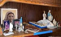 Wide view of wooden shelf with various religious statues, framed prints, and small figurines arranged