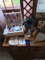 Full view of table top including sewing box, hand mirror with broken handle, napkins, decorative ribbon basket, and various small cologne bottles