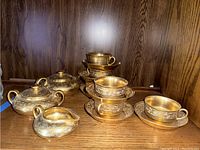 Full view of tea set items including cups stacked inside saucers, sugar bowl with lid, creamer, and part of teapot visible.