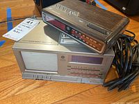 Two vintage GE clock radios stacked: an analog AM/FM dial clock radio combo on top and a digital clock radio underneath with a coiled power cord.
