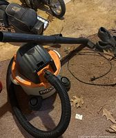 Orange and black Ridgid wet/dry vacuum with hose and wand attachment on concrete floor.
