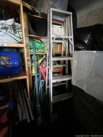 Aluminum step ladder stored vertically among other household items, visible wear and stains on steps and frame.