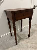 Full view of the antique mahogany bedside table showing turned legs, rectangular removable top, and front drawer.