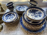 Grouped view of various plates, bowls, and cups displaying the blue and white Willow pattern stacked together showing wear and patina from use.